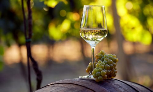 A glass of white wine with grapes on a barrel